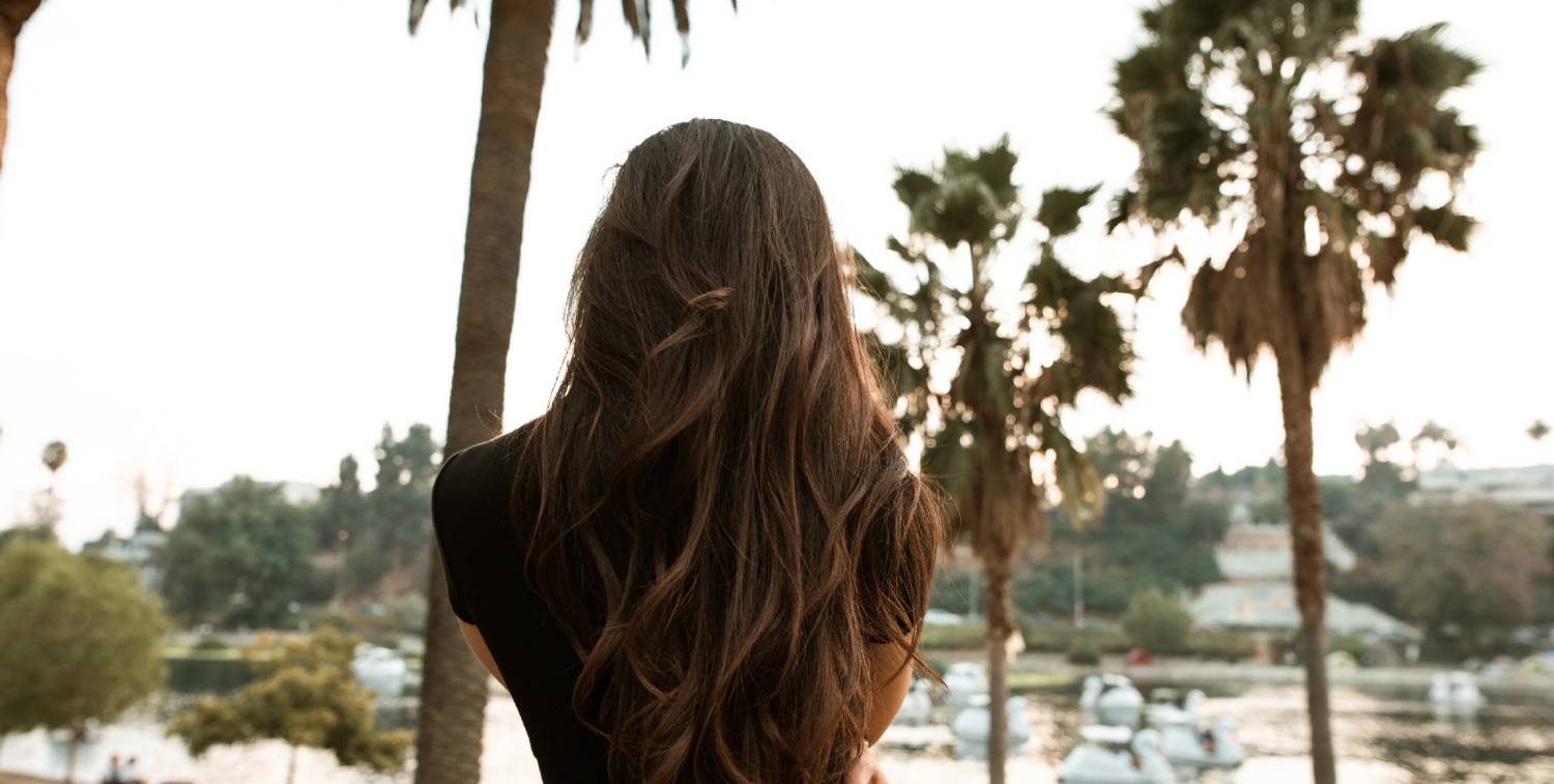 A woman with thick long hair seen from behind. Beach, coastal background. Concept of hair loss, hair thickening shampoos, KeraFiber shampoo.