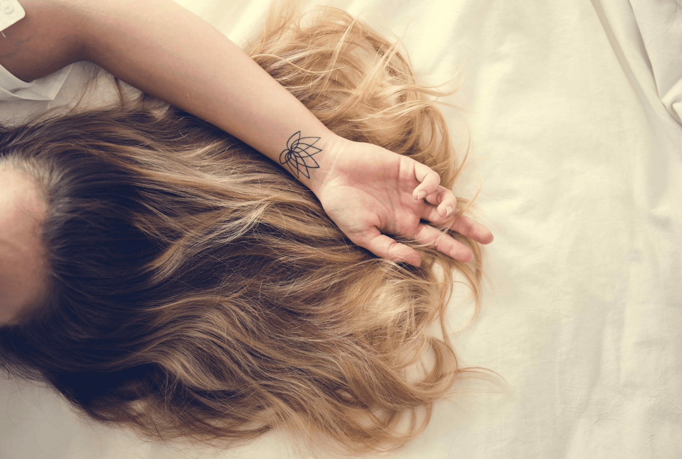 A faceless woman with thick hair lying on a bed.